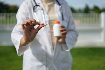 Doctor with stethoscope who is standing in Hospital garden  is holding an medicine bottle to assess...