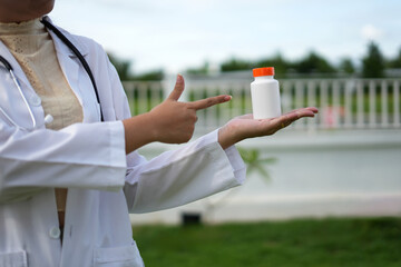 Doctor with stethoscope who is standing in Hospital garden  is holding an medicine bottle to assess...