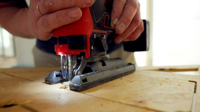 Person using the jigsaw power tool. the worker is holding jigsaw with the both hands, guiding it along marked lines on a wooden board. 