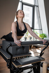 Woman training pilates on the reformer bed. Reformer pilates studio machine for fitness workouts in gym. Fit, healthy and strong authentical body. Fitness concept