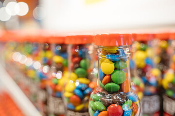 Clear bottles filled with colorful candies line up on the shelf. The perspective creates a bokeh effect in the background.