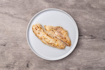 Grilled tilapia or saint peter on a plate isolated over wooden table