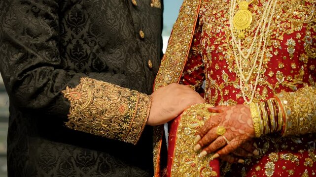 Wedding couple hands while holding each other, they dressed in the traditional red and black Asian clothes, Elements of hindu wedding. Close up