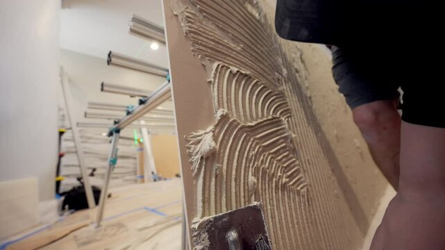 Professional construction worker applies thick layer of adhesive to the ceramic tile to glue it to the wall. 