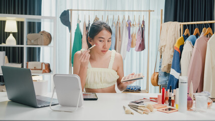 Young beautiful Asia lady blogger looking at camera recording swatch apply eyeshadow palette on skin show review to follower product vlog video live streaming at home. Business online media concept.