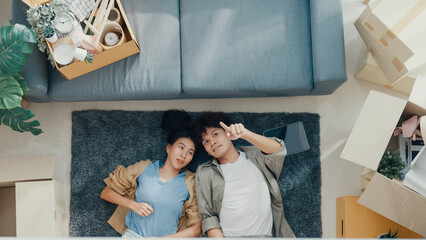 Top view. Happy Asian couple lay down and relax on carpet share idea for decoration furniture in empty area on living room at new house. Husband wife move house, Apartment Rent And Ownership Concept.