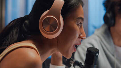 Close-up Young happy Asia couple wear headphone sit on desk online live streaming football live score watch soccer sport game on laptop use microphone talk with follower small studio in home at night.