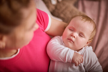 Young adult mother with short hair gently cradles infant baby girl. Soft lighting creates warm, calm atmosphere. Focus on baby peaceful expression while sleeping