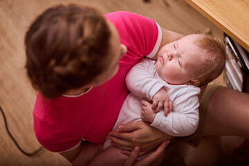 Young woman with brown hair cradles infant girl, evoking warmth and comfort. Soft indoor light highlights intimate moment, creating serene atmosphere around them