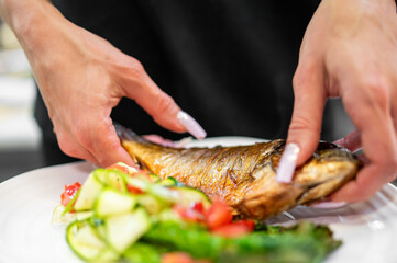 Hands holding a plate with grilled fish and a fresh vegetable salad, featuring zucchini ribbons and diced tomatoes. A bright, appetizing presentation of a healthy homemade meal.