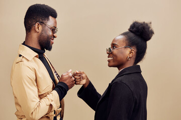 Happy couple sharing a playful moment, dressed in stylish casual outfits with sunglasses, against a neutral beige background in a warm color palette