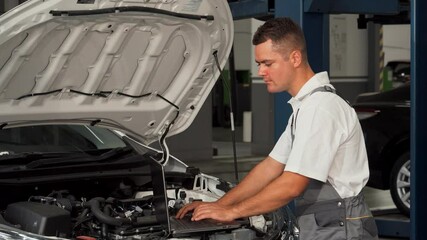 Cheerful mechanic using laptop while expertly repairing a car