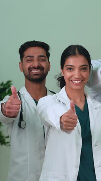 Vertical video. Two indian doctors, a man and a woman, stand side by side, smiling at the camera and giving a thumbs-up gesture, expressing positivity and approval in a hospital setting