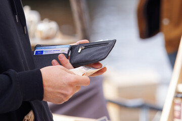 A close-up view of a person holding a wallet with cash while outdoors. Captures the concept of...