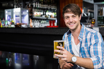 Smiling man raising glass beer mug while sitting on glossy bar counter at pub, copy space
