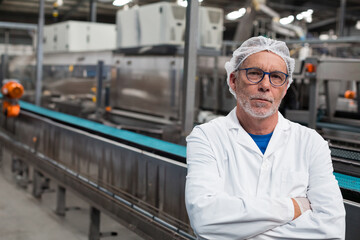 Senior man wearing protective attire inspecting conveyor belt in manufacturing plant, copy space