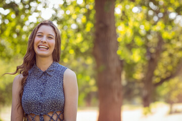 Teenage girl standing in sunlit park wearing blue floral top with lace-up waist cutouts, copy space