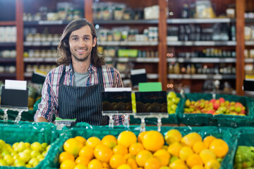 Mid adult male vendor standing behind green crates of oranges at grocery store with chalkboard tags