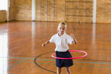 Girl spinning bright pink hula hoop in school gymnasium with colored court lines on hardwood floor