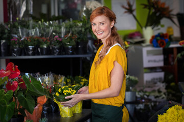 Yellow flowering plant sitting on shop counter beside anthuriums, with shelves of wrapped bouquets