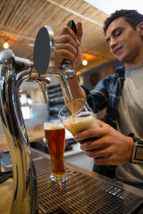 Hispanic male bartender pouring amber beer from metal tap handle on bar counter with rubber mat
