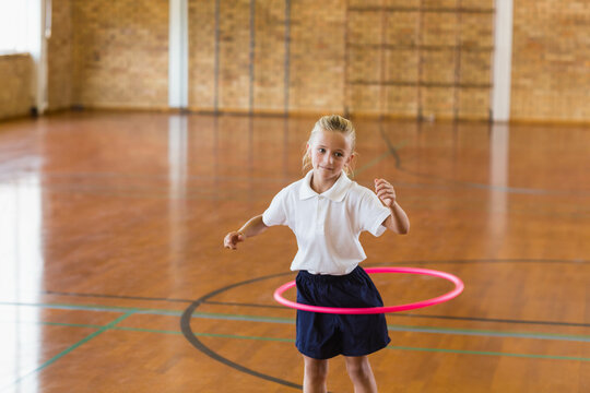 Fototapeta Girl spinning bright pink hula hoop in school gymnasium with colored court lines on hardwood floor