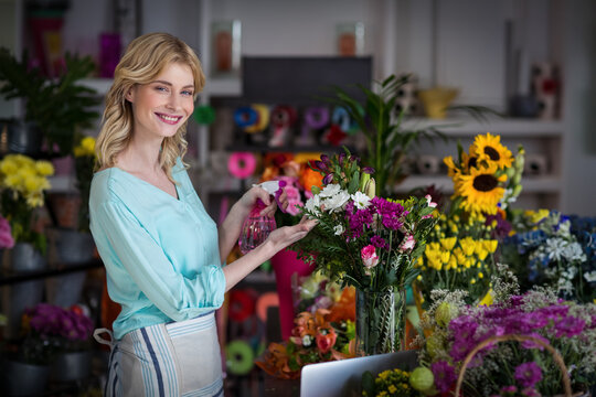 Florist misting flowers in glass vase with pink spray bottle and sunflowers, tulips at shop counter