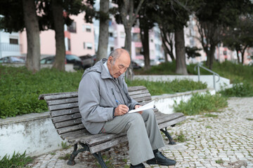 Fototapeta premium Senior man writing on a bench in the park