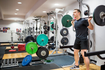 Obraz premium Adult man performing back squat in squat rack at gym with barbell and plates, copy space