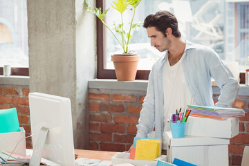 Man standing at cluttered desk examining computer monitor in brick office, copy space
