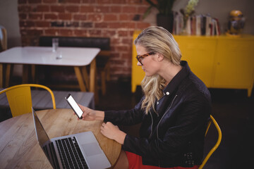 Smartphone resting near open laptop on table with yellow storage cabinet in coworking space