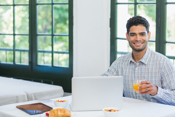 Male office worker holding glass of orange juice while using laptop at breakfast table, copy space © wavebreak3
