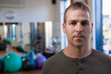 Mid adult male wearing olive shirt standing in gym with stability balls and mirror, copy space