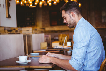 Man sitting at wooden table in coffee shop wearing striped shirt holding white cup, copy space