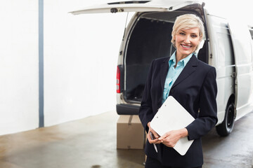 Woman in suit holding clipboard, noting details at warehouse bay beside white cargo van, copy space © WavebreakMediaMicro