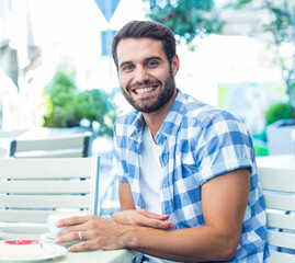 Bearded man in plaid shirt sitting at garden patio table holding coffee cup with fruit cake