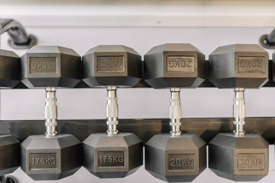 Close-up view of hexagonal dumbbells arranged on a rack in a gym setting, showing weights from 12.5kg to 20kg..