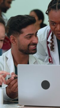 Vertical video. Medical professionals reviewing patient information on laptop, working together in modern hospital setting with diverse colleagues