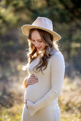 A beautiful pregnant woman is posing gracefully amidst a lush green setting, radiating immense joy and tranquility