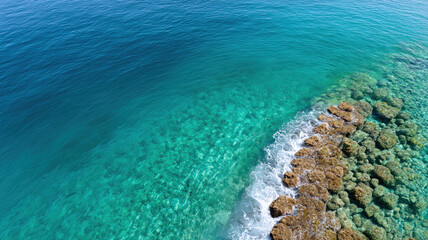 Aerial view of vibrant coral reef in turquoise sea, with waves gently crashing on rocks, showcasing beauty of marine life and clear water