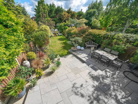 Aerial shot of beautiful English garden in spring with Indian sandstone patio and attractive shrubs, outdoor dining area and blue sky.