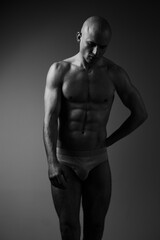 Fototapeta premium Black and white image of a muscular man posing gracefully, showcasing strength, confidence, and vulnerability in a simple yet captivating composition.