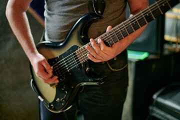 Musician playing an electric bass guitar at music rehearsal, practicing guitar technique in dimly...