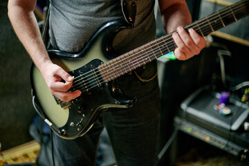 Obraz premium Musician playing an electric bass guitar at music rehearsal, practicing guitar technique in dimly lit setting, close up view guitarist hands