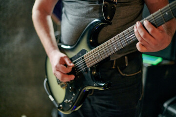 Musician playing an electric bass guitar at music rehearsal, practicing guitar technique in dimly...
