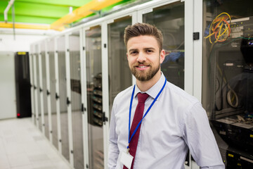 Male IT professional wearing light shirt, red tie inspecting server rack in data center, copy space