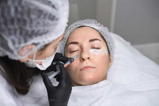 Young woman in medical clinic receives facial injection. Sterile, clinical atmosphere emphasizes precision and care, highlighting focus on beauty enhancement, top view
