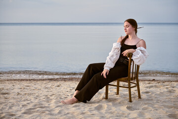 Young woman relaxing on wooden chair by calm seaside, evoking serene contemplation. Setting conveys...