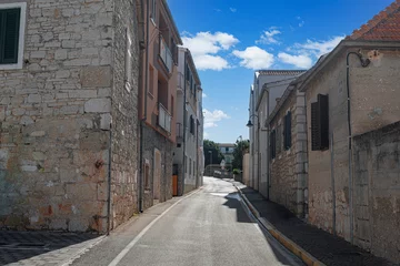 A quiet, sunlit street in the old town of Primosten, Croatia, lined with traditional stone buildings and Mediterranean charm.