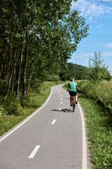 Fototapeta premium Elderly adult rides bicycle along serene park trail, surrounded by lush greenery under blue sky